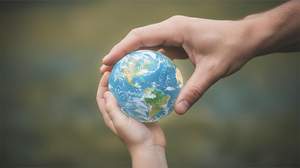 Hand hält eine Weltkugel und eine Kinderhand ist ausgestreckt